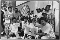 Group photo of workers with protest signs holding up clenched fists from David Bacon's Trabajadores Immigrantes/<br />
Immigrant Workers