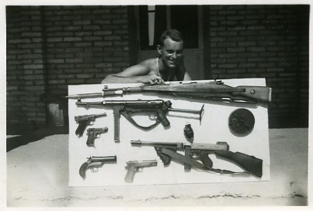 Man smiling proudly while showing off his collection of guns