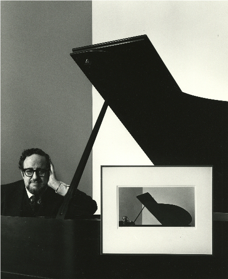 Arnold Newman self portrait, posed next to a piano and his framed portrait of Igor Stravinsky