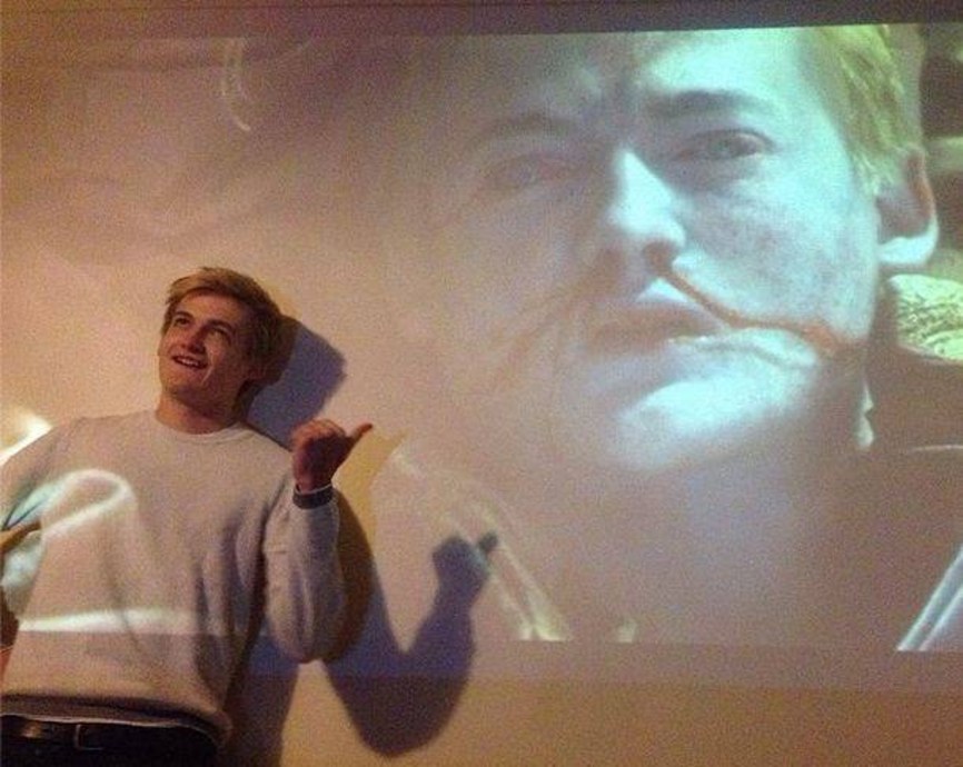 Picture of Jack Gleeson standing in front of a screen, on which Joffrey Baratheon (played by Gleeson) is shown dead, blood streaming from his nose