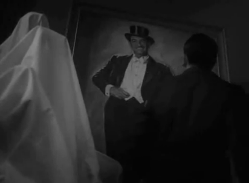 George Valentin here stands with his back to the screen, facing his full-length portrait.  In the portrait, Valentin wears a 1920s style mustache and is wearing a top coat and tails, as well as a top hat.