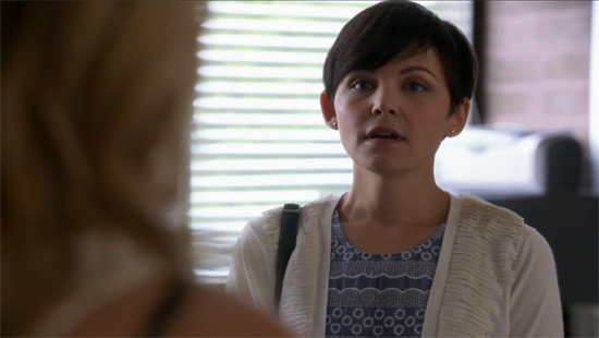 Mary Margaret, a character from Lost, stares at the camera. She wears a blue patterned dress beneath a thin white sweater jacket.