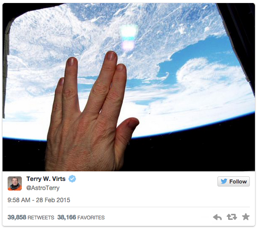 A hand makes the Live Long and Prosper sign against a window of the International Space Station.