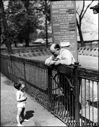Man and child on either side of an early twentieth century park fence