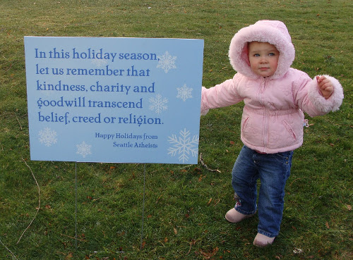 Little girl stands next to sign that reads: "In this holiday season let us remember that kindness, charity and goodwill transcend belief, creed or religion.  Happy Holidays from Seattle Atheists." 