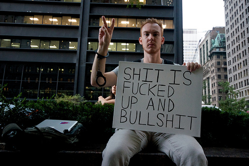 Protester holding a sign that reads "SHIT IS FUCKED UP AND BULLSHIT" "