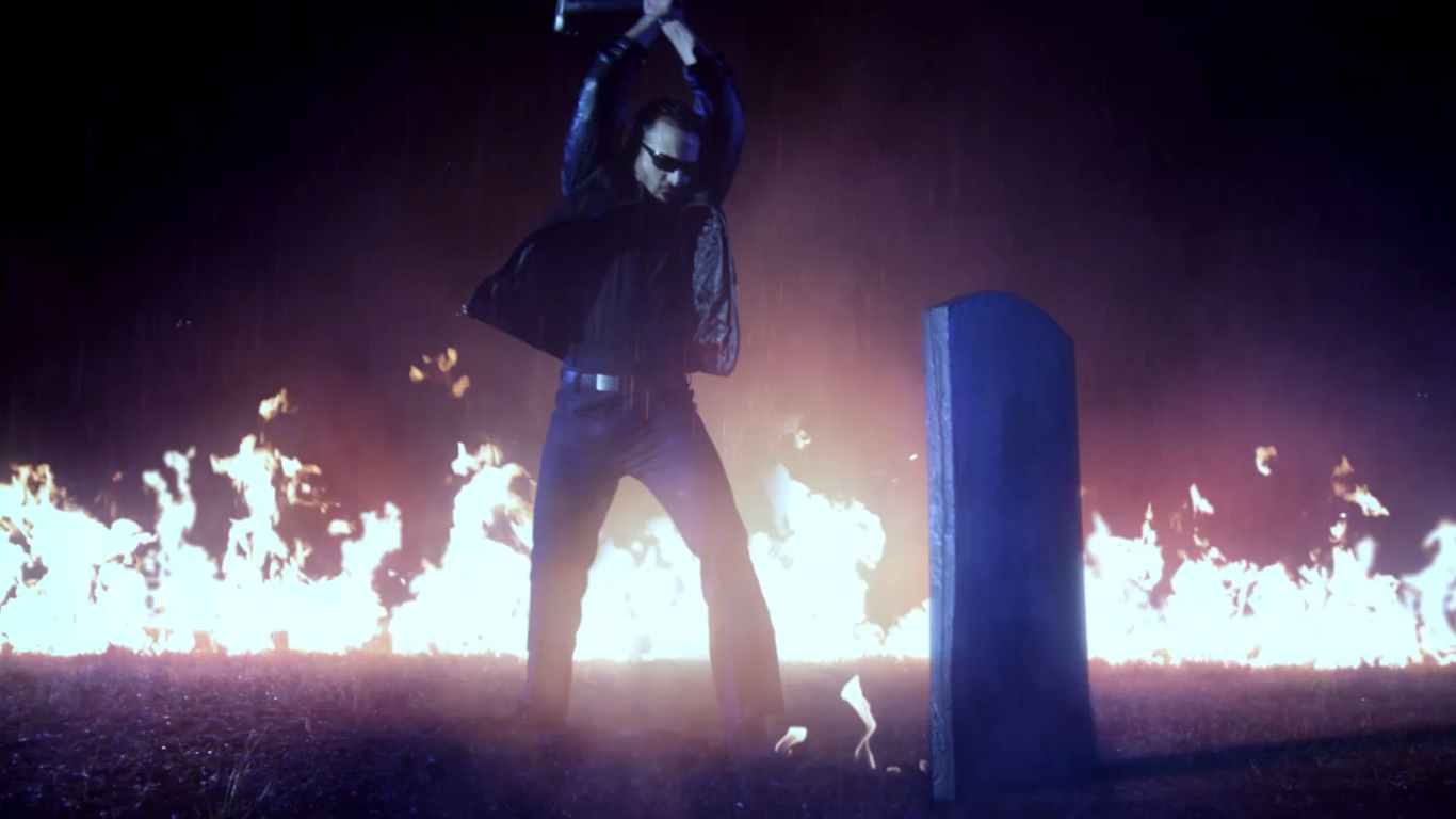 Jamie Casino uses a sledgehammer on his brother's grave as flames illuminate the background.