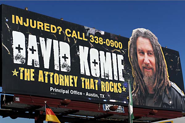 Picture of David Komie billboard, which features the lawyer wearing a leather jacket, black t-shirt, and dreadlocks