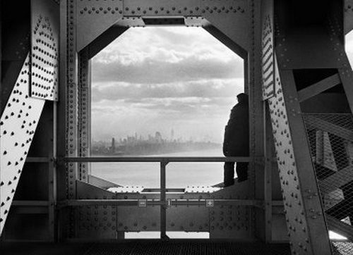 Man looks out from girders of George Washington Bridge at Manhattan skyline framed by bridge girders