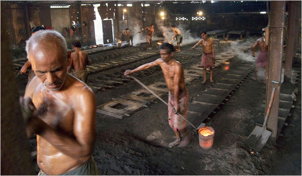 Foundry Workers wearing only cloth wraps carrying molten metal to the manhole molds