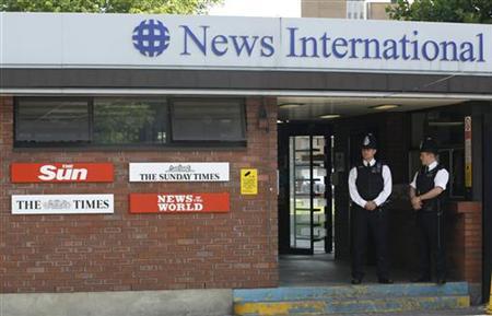 This image depicts two English bobbies standing outside the offices of The Sun, Rupert Murdoch's British newspaper.  The police stand on the right side of the image, one facing towards the camera, one angled to look at his colleague.
