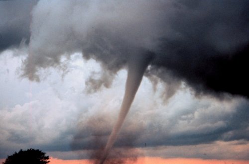 Tornado touches down in the countryside against dark sky; sliver of pink sky visible near horizon