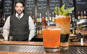 two drinks on a bar with a bartender looking on--one has shaved ice and the other a block